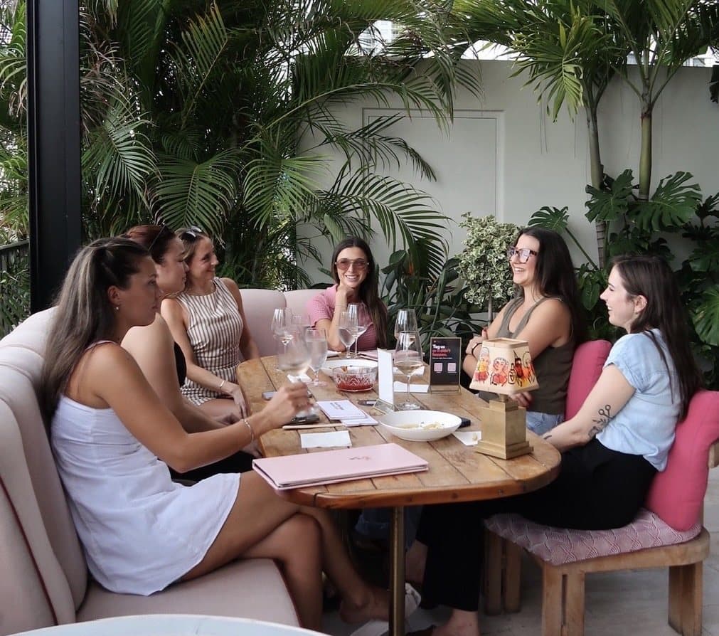 A Walk & Wine group around a table on a plant-filled Miami terrace, mid-conversation over wine.